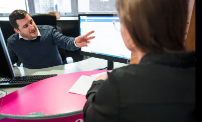 A person pointing at a computer screen to another person